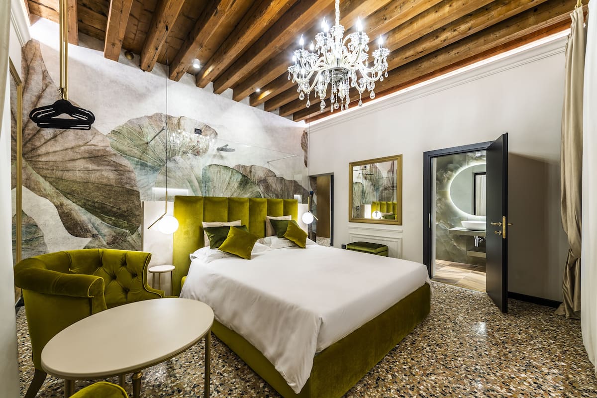 Une chambre d’hôtel moderne avec un grand lit, un fauteuil vert et une petite table.