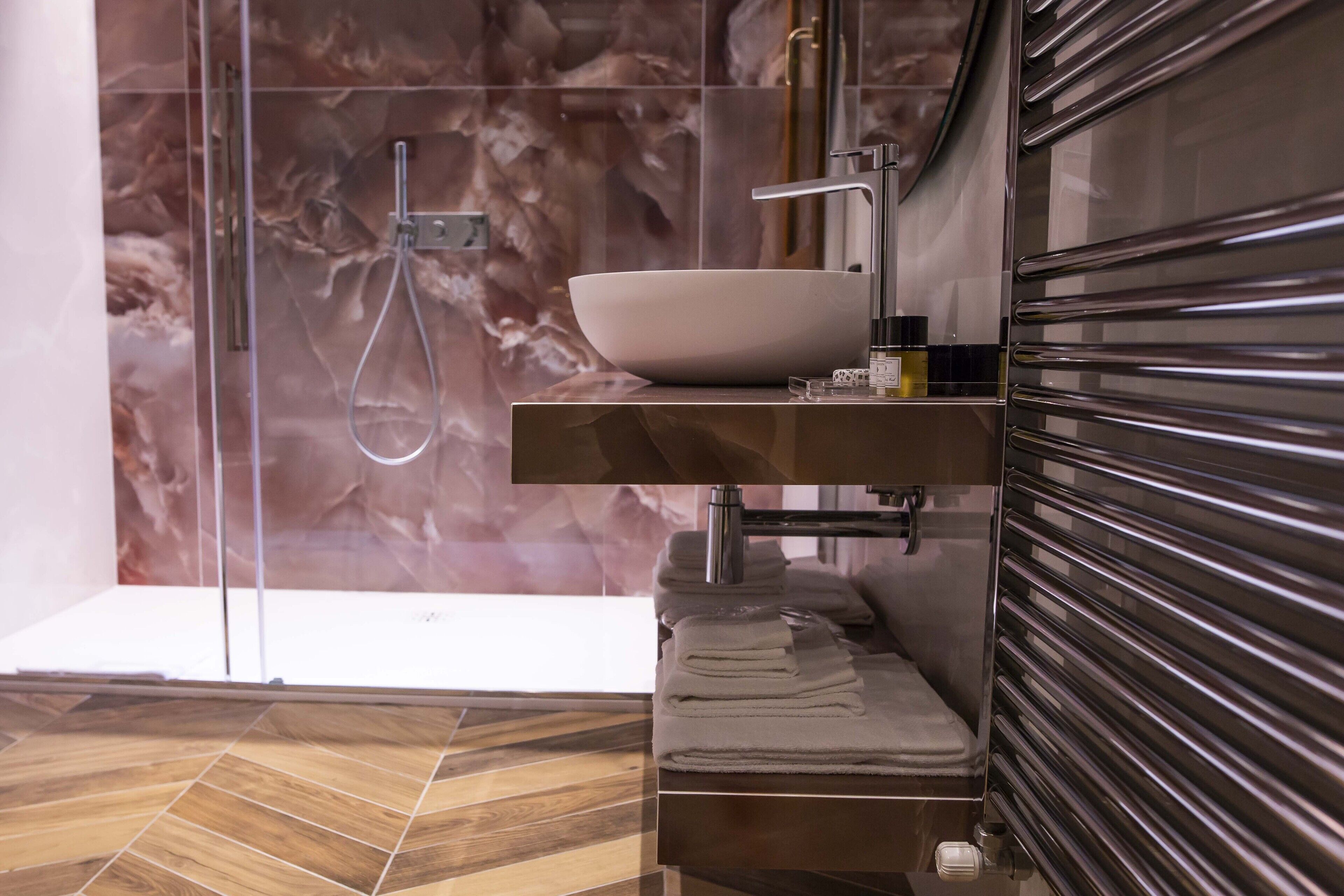 A modern bathroom with a large white sink, a glass shower enclosure, and a wooden floor.
