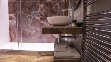 A modern bathroom with a large white sink, a glass shower enclosure, and a wooden floor.