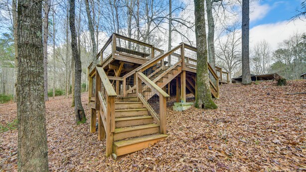 A wooden cabin with a staircase leading to a deck, surrounded by trees and a leaf-covered ground. - Creek Lodge  - LaGrange's Best Kept Secret (LaGrange)