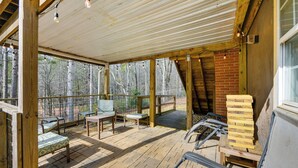 A covered outdoor deck with wooden furniture, a brick wall, and a view of trees. - Creek Lodge  - LaGrange's Best Kept Secret (LaGrange)