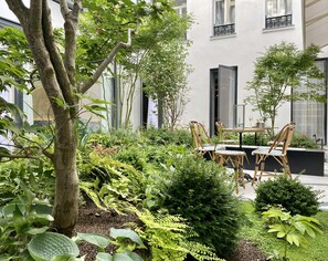 An outdoor seating area with tables and chairs, surrounded by various plants and trees.