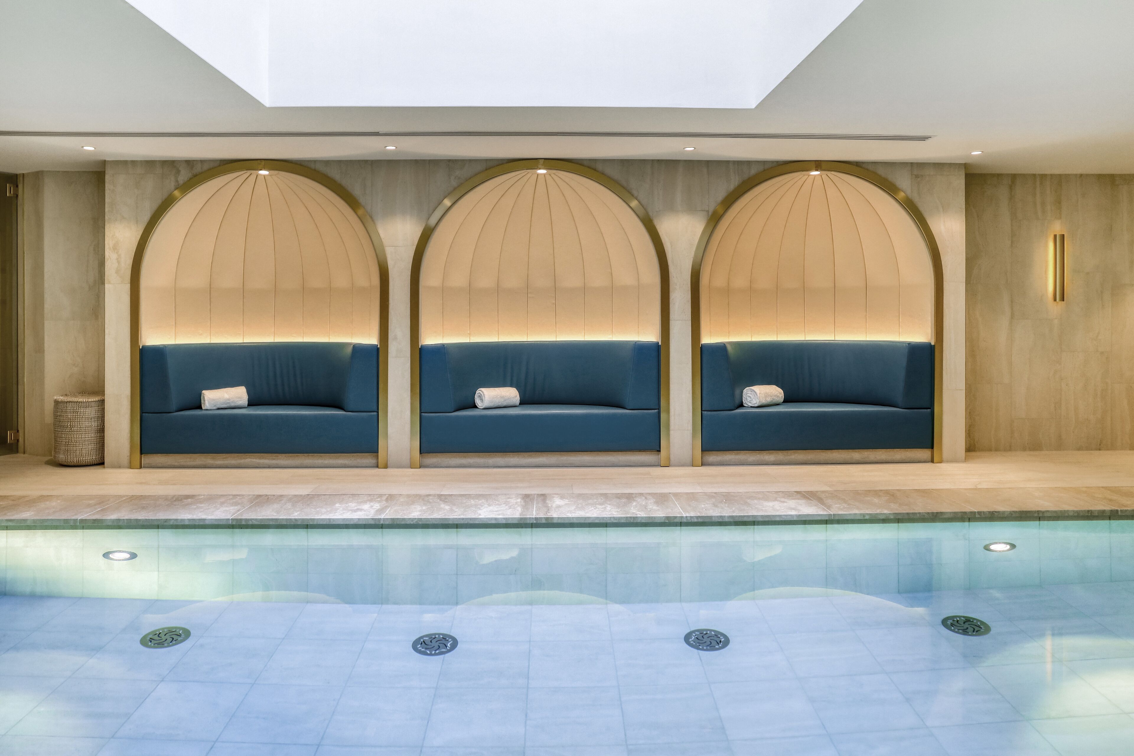 A pool area with three blue sofas under arched alcoves, a clear pool, and a tiled floor.