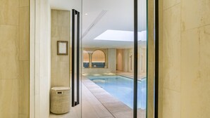 A modern indoor swimming pool area with a glass partition, a framed certificate on the wall, and a wicker basket on the floor. - Maison Albar Hotels Le Vendome (Paris)