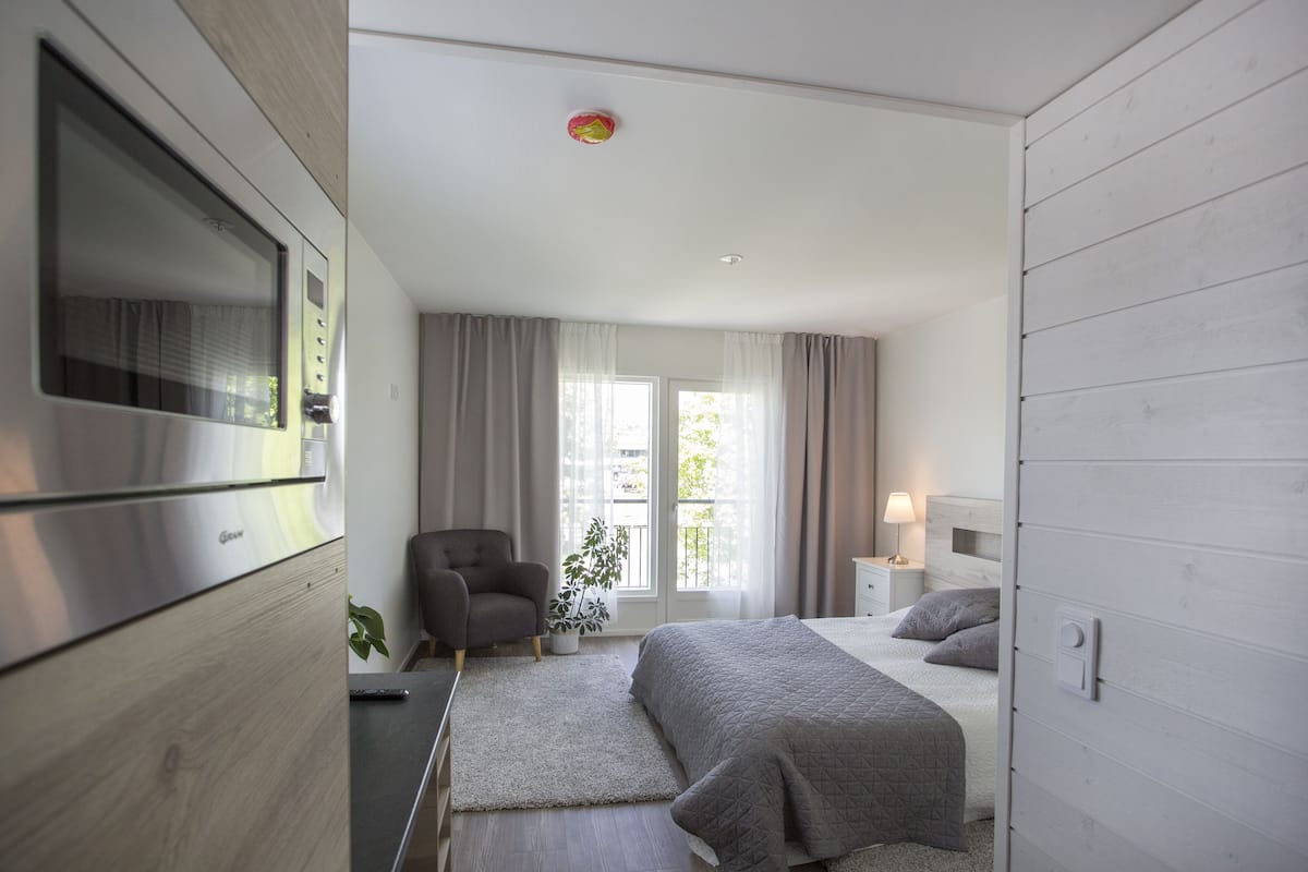 Ein modernes Schlafzimmer mit einem Bett, einem Sessel, einem Schreibtisch und einem Fenster mit Vorhängen.