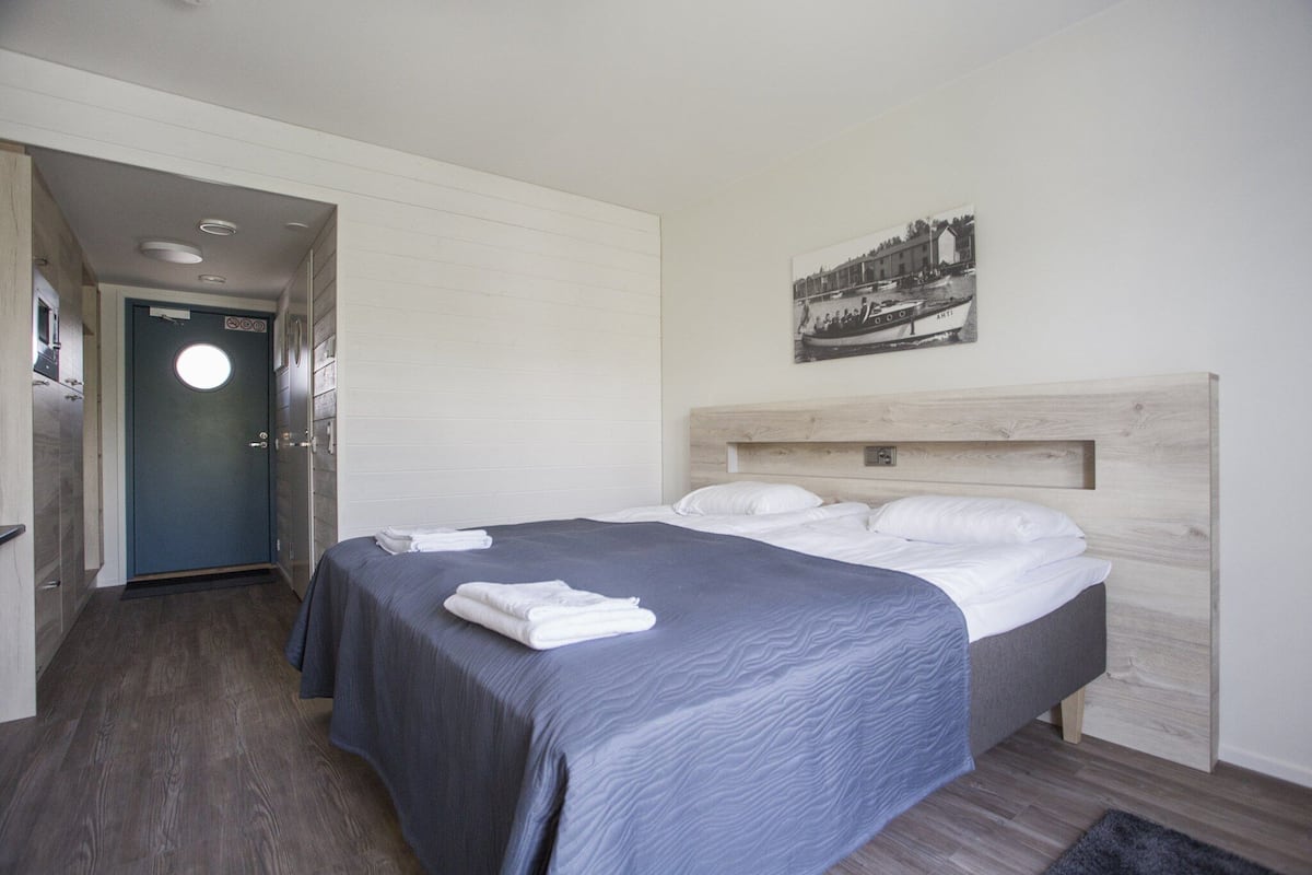 Ein Hotelzimmer mit einem Bett, einem Holzkopfteil, einem an der Wand befestigten Bild und einer Tür zu einem Flur.