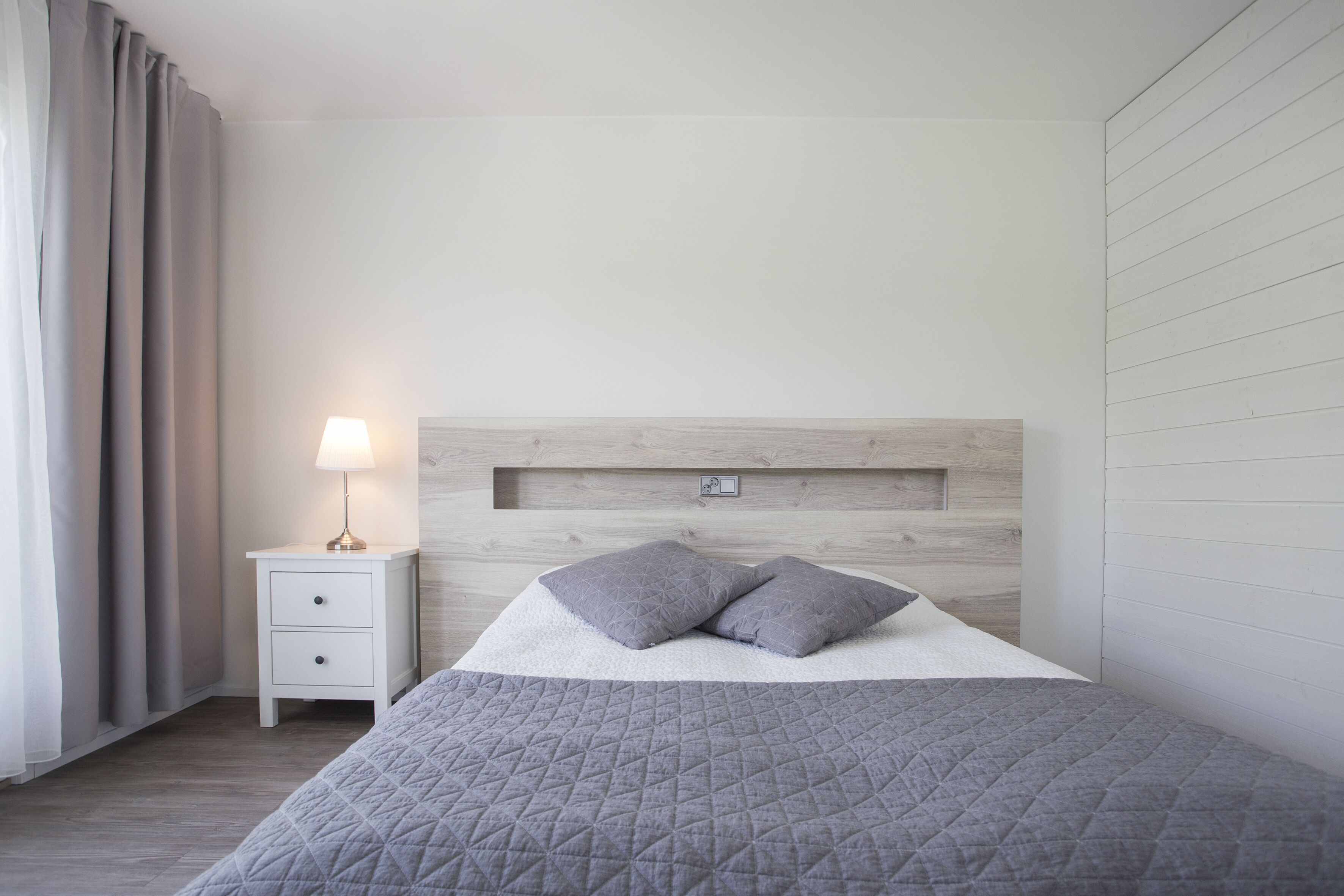 A neatly arranged bedroom with a bed, a bedside table with a lamp, and a headboard.