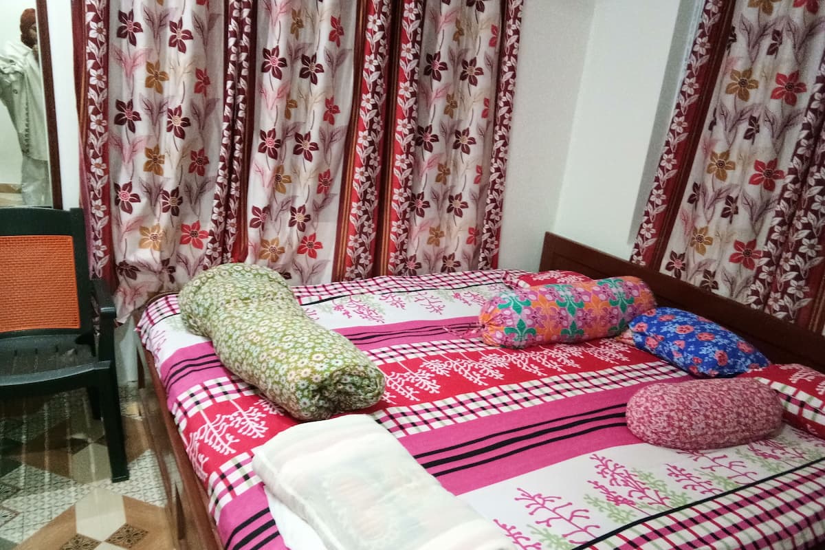 A bed with floral-patterned bedding, a green rolled-up blanket, and multiple pillows.