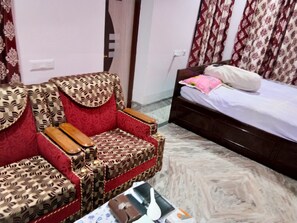 A room with a patterned armchair, a bed with a pink pillow, and a marble floor.