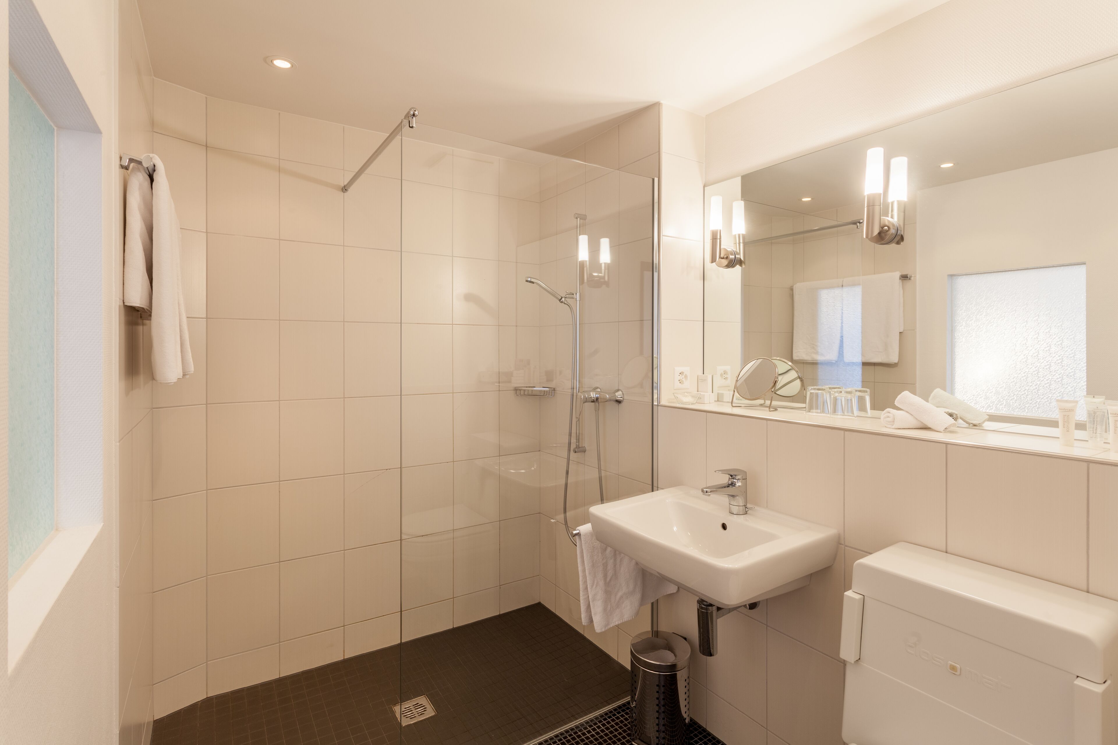 A modern bathroom with a glass-enclosed shower, a white sink, and a large mirror.