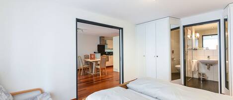 Un dormitorio con cama, una silla, un armario y un baño visible a través de una puerta abierta.