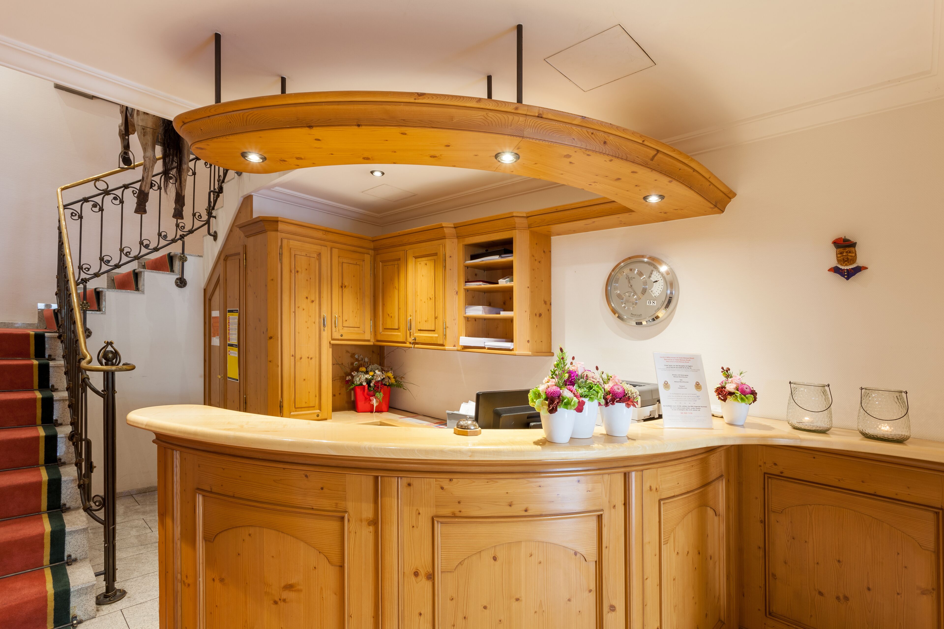 A kitchen with wooden cabinets, a curved wooden ceiling, a clock on the wall, and a staircase with red steps.