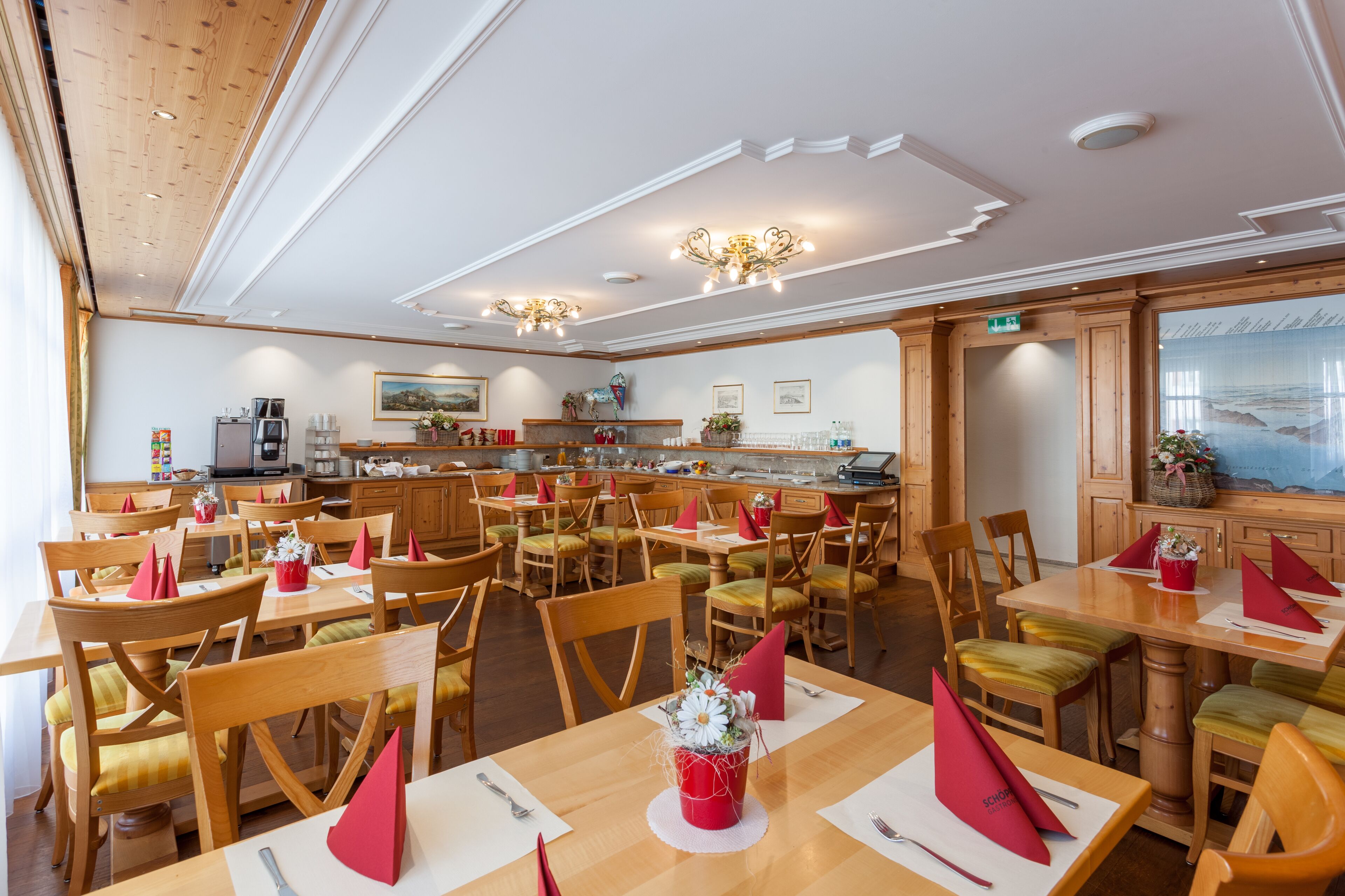 A restaurant with wooden tables and chairs, a kitchen area, and a painting on the wall.