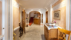 A hallway with a wooden staircase, a reception desk, and a dining area with a table set for two. - Weisses Rössli Swiss Quality Hotel (Ingenbohl)