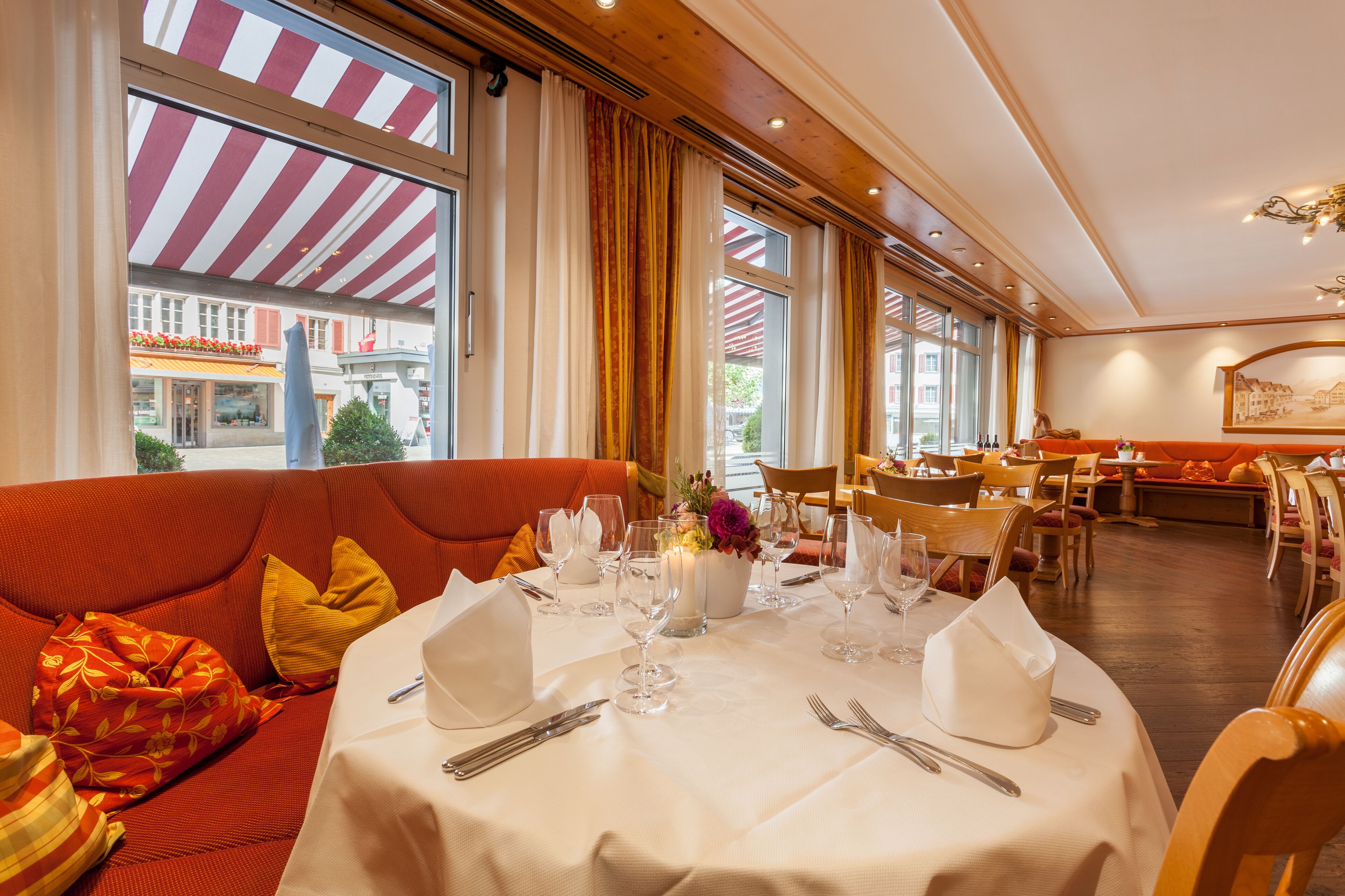 A dining area with a table set for four, a sofa with cushions, and large windows with striped awnings.