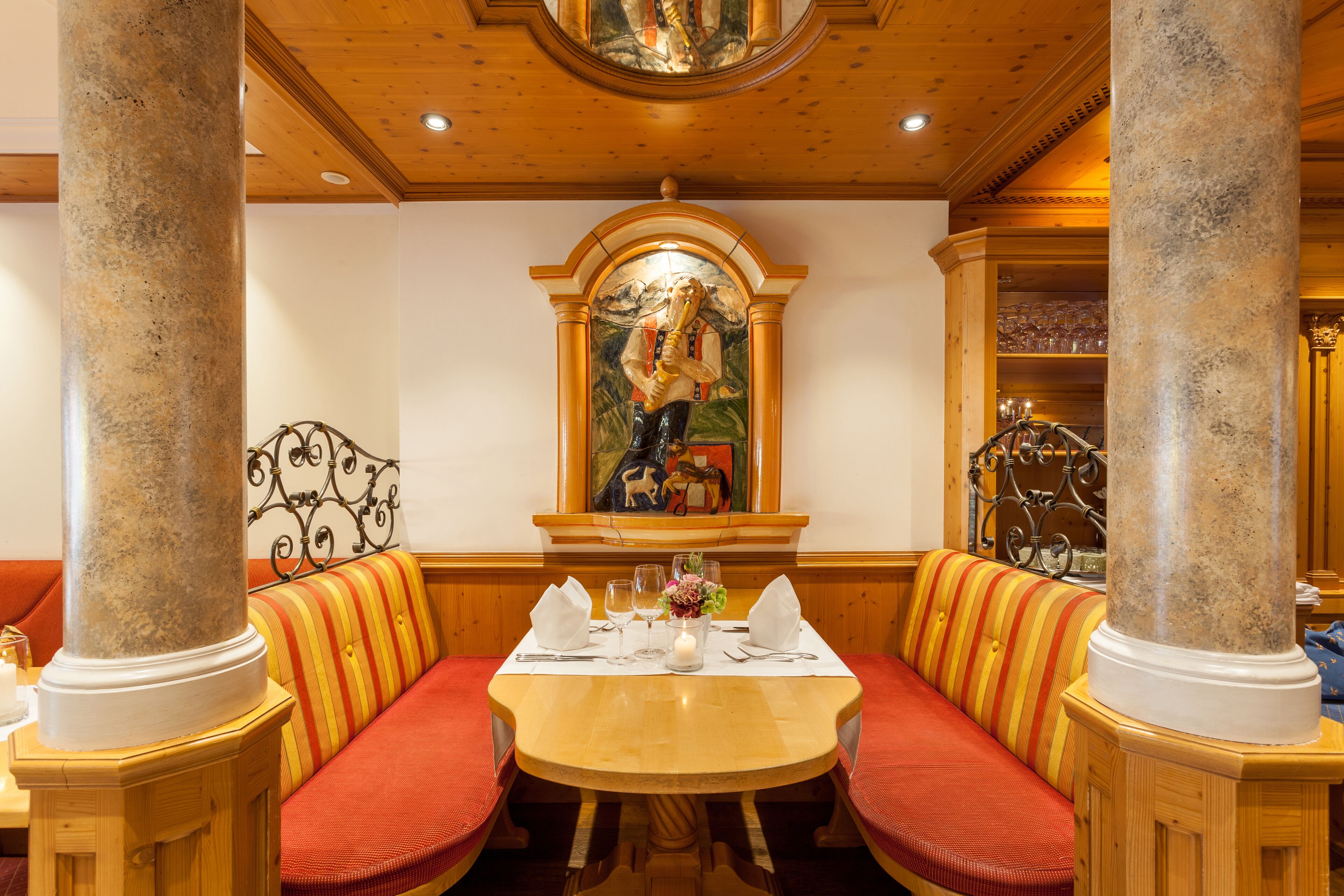 A dining area with a round table, striped booth seating, and a mural on the wall.
