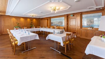 Un salón de conferencias con largas mesas, paneles de madera y ventanas amplias con vistas a la montaña.