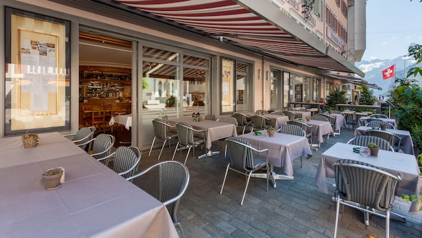 An outdoor café with tables and chairs, a Swiss flag, and a mountain view. - Weisses Rössli Swiss Quality Hotel (Ingenbohl)