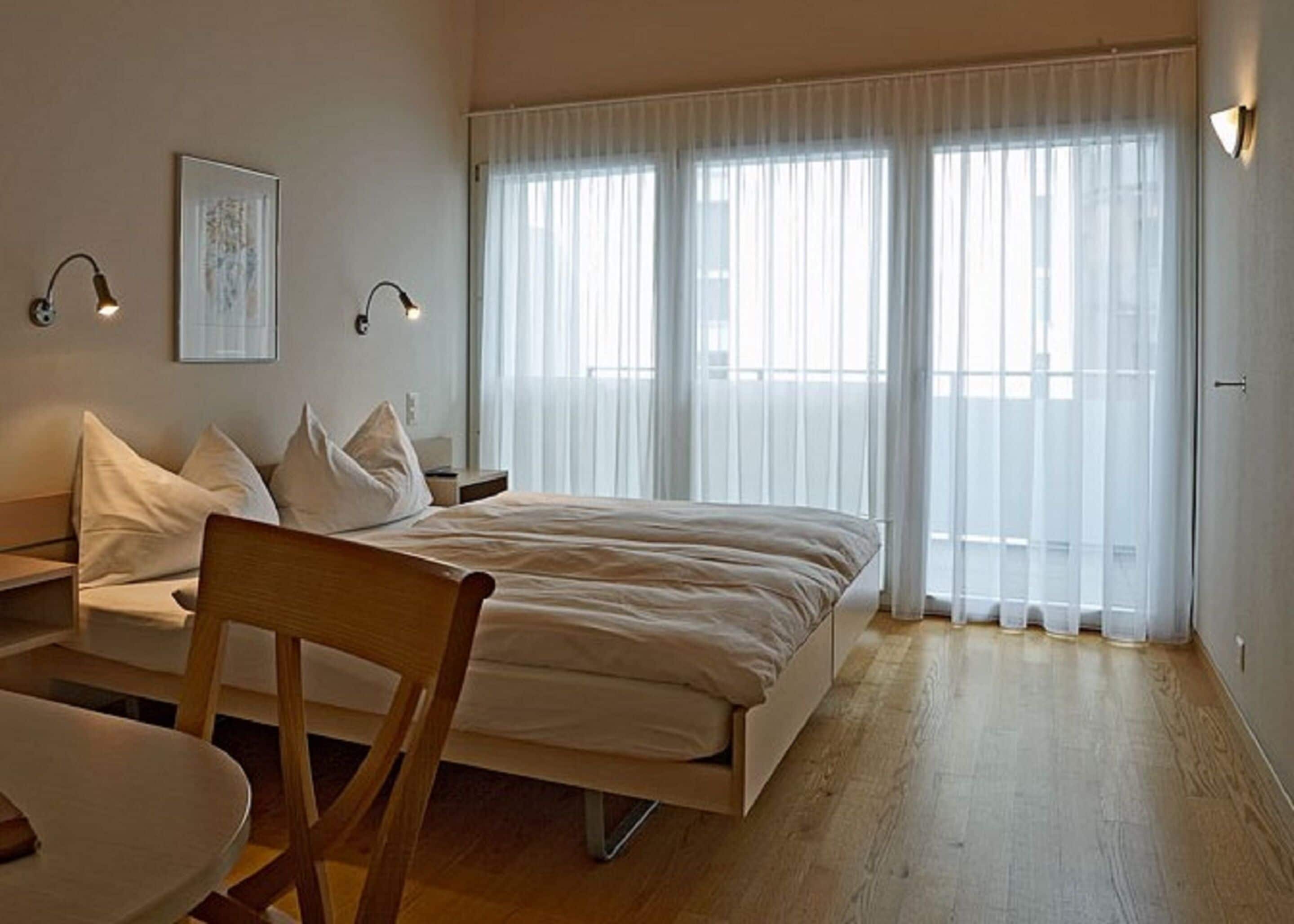 Ein Schlafzimmer mit einem Bett, einem Sessel, einem Tisch und zwei Nachttischlampen.