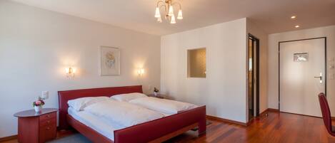 Un dormitorio moderno con cama roja, suelo de madera e iluminación empotrada.