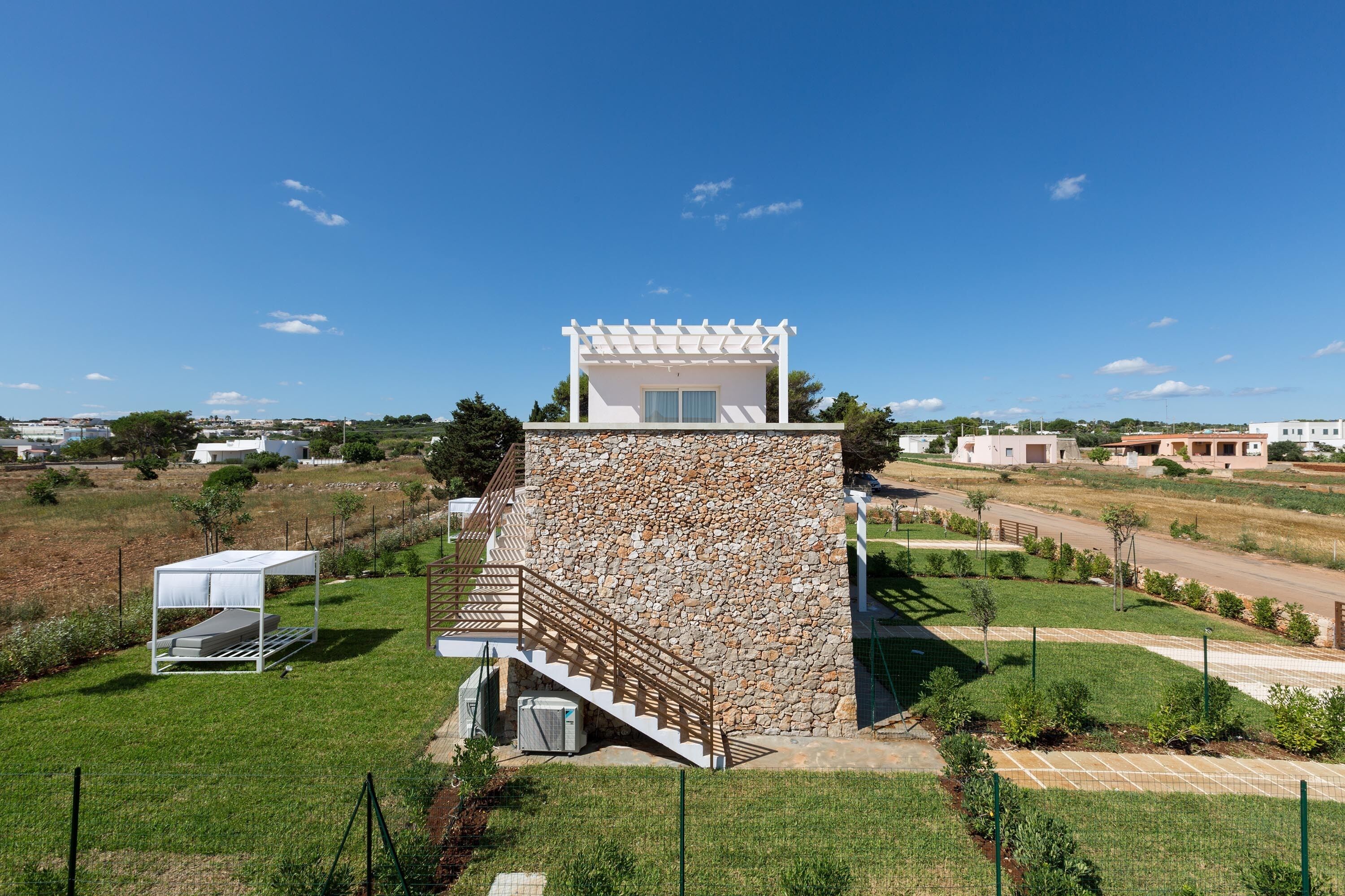 A modern building with a stone facade, a small balcony, and a staircase leading to a flat roof.