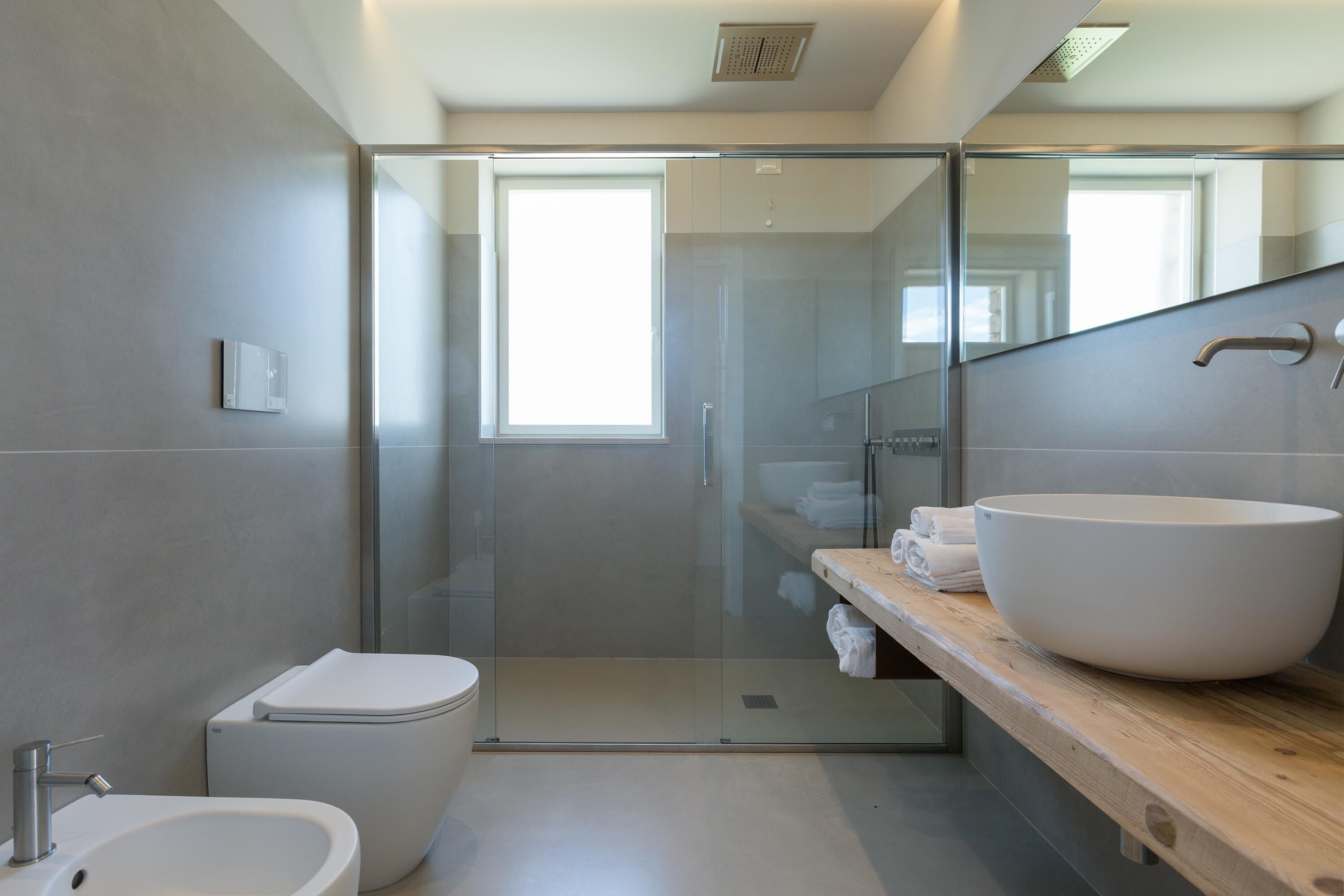 A modern bathroom with a glass-enclosed shower, a large white sink, and a wooden vanity.