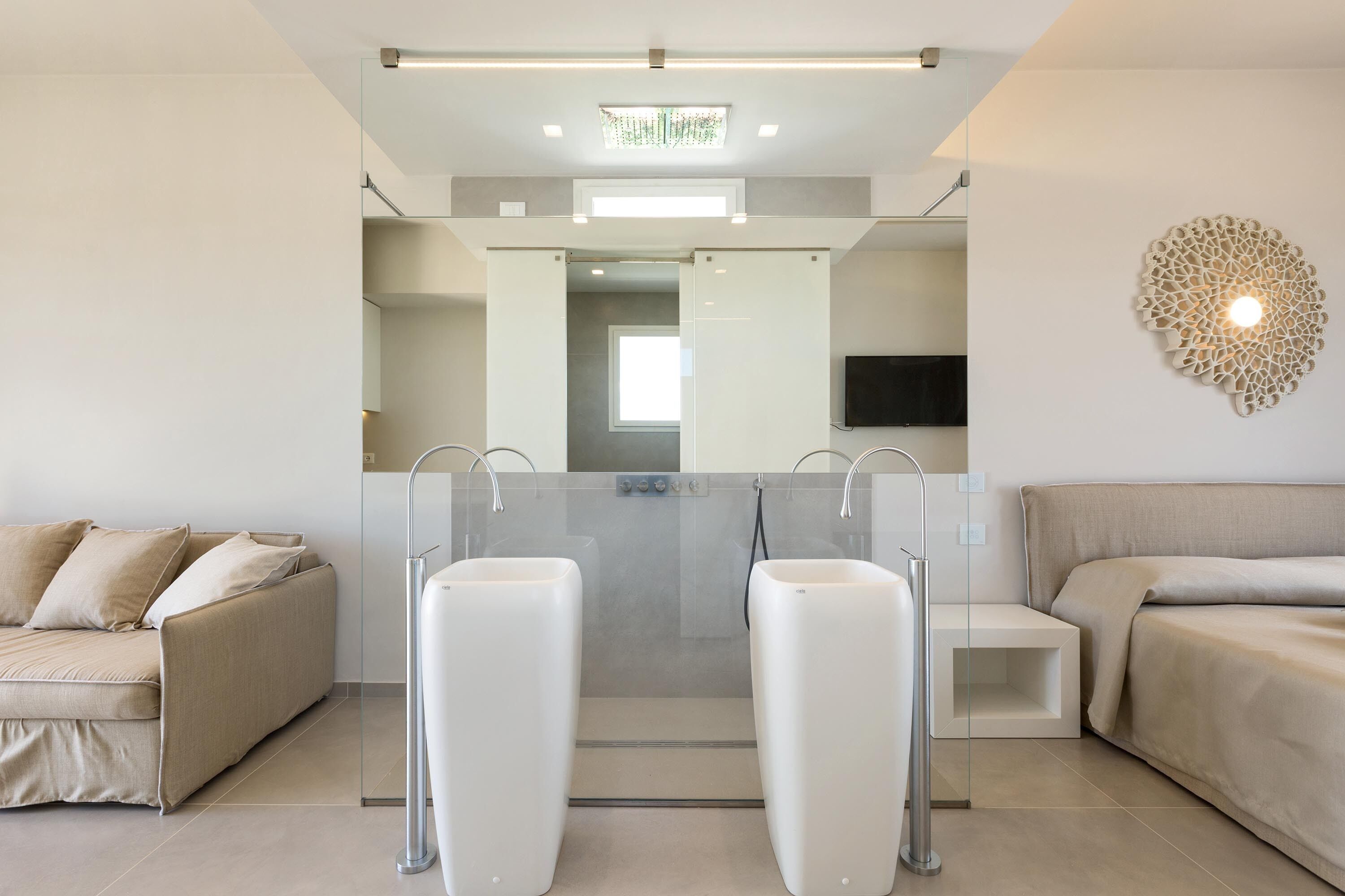 Un baño moderno con mampara de vidrio, un sofá y un televisor en la pared.