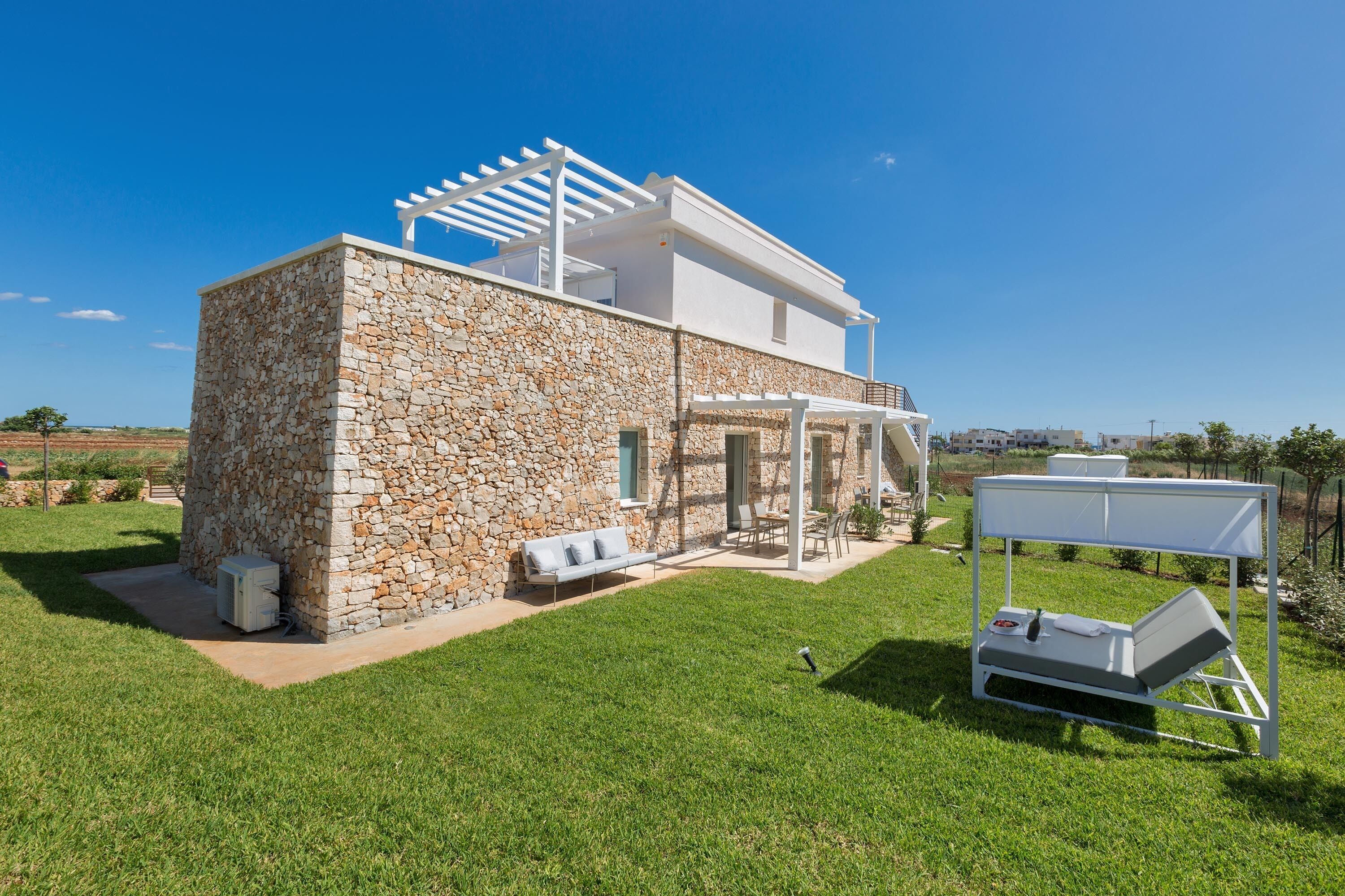 A modern house with stone walls, a white exterior, and a covered outdoor seating area.
