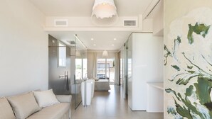 A modern, well-lit hotel room with a sofa, a bed, a bathroom with a glass shower, and a large abstract painting on the wall. - Perla Saracena Luxury Suites (Salve)