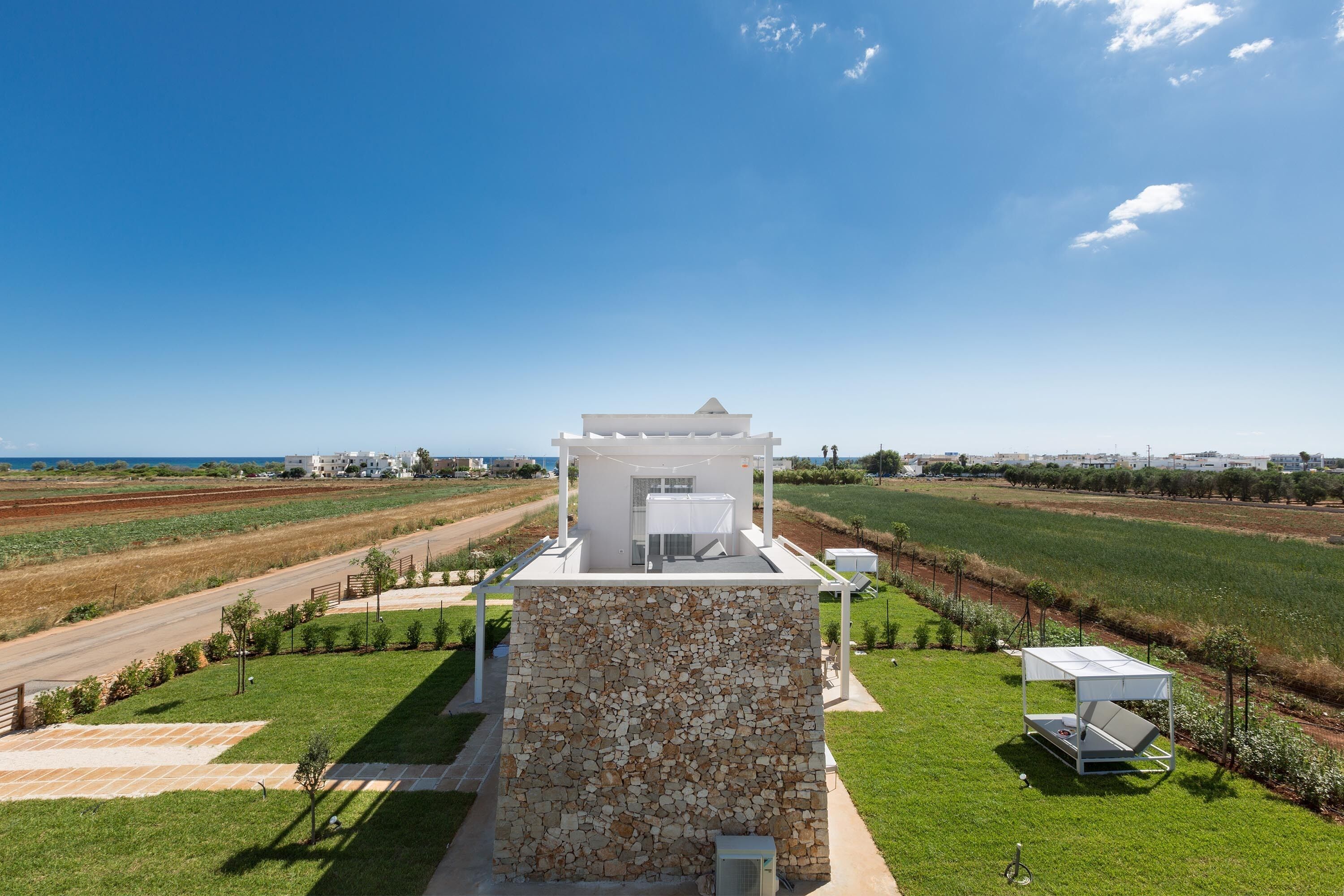 A modern villa with a stone facade, a covered outdoor seating area, and a view of the surrounding fields.