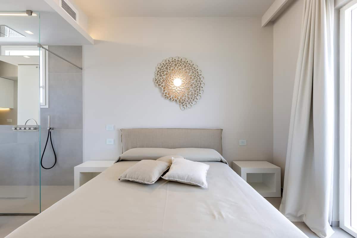 Ein modernes Schlafzimmer mit einem großen Bett, einer Wandleuchte und einer Duschkabine aus Glas.