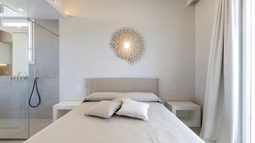 Une chambre à coucher moderne avec un grand lit, un luminaire fixé au mur et une cabine de douche en verre.