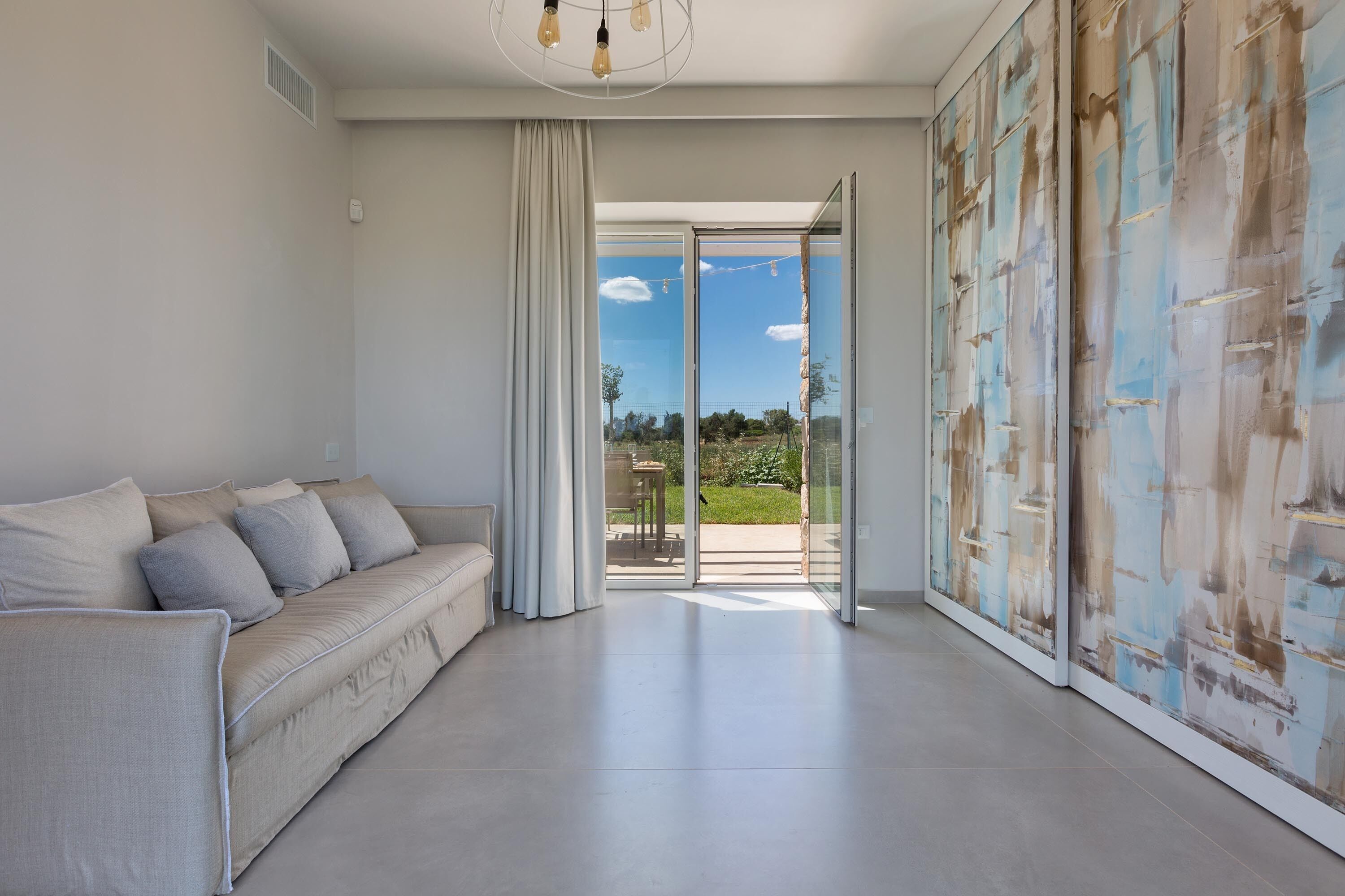 A modern living room with a sofa, a sliding glass door leading to an outdoor area, and a large abstract painting on the wall.