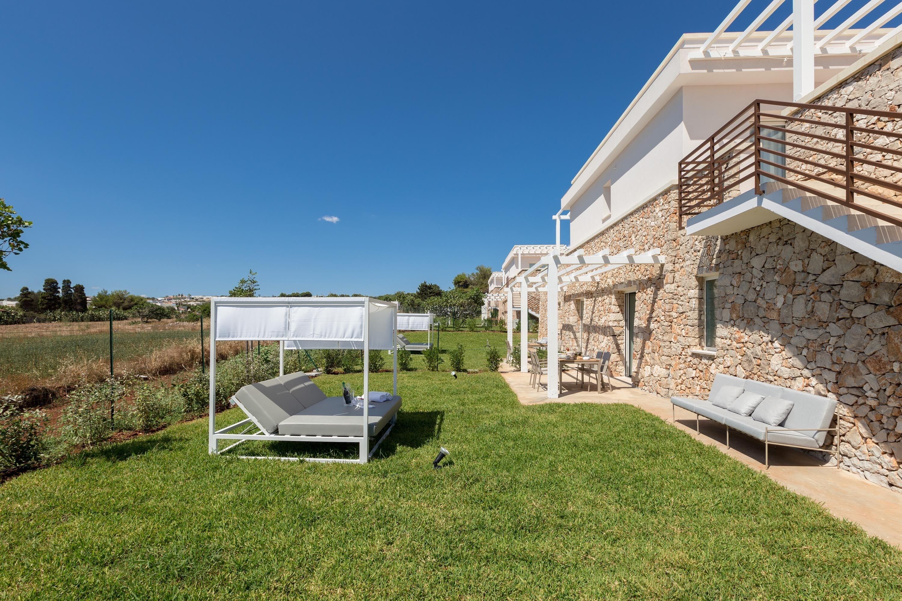 Un espacio moderno al aire libre con un toldo blanco, una pared de piedra y un cielo azul despejado.