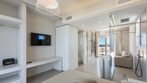 A modern hotel room with a large bed, a TV, a glass shower enclosure, and a balcony view. - Perla Saracena Luxury Suites (Salve)