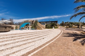 A stone staircase leading to a pool area with a modern building in the background.