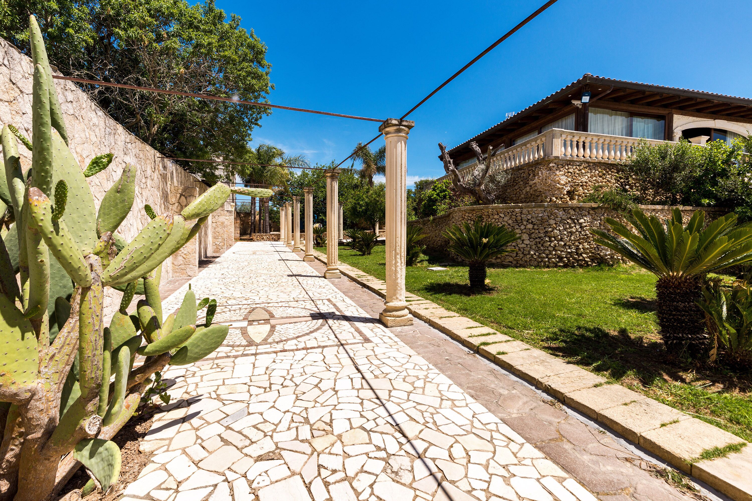 A cobblestone pathway leading to a building with a stone facade and a balcony.