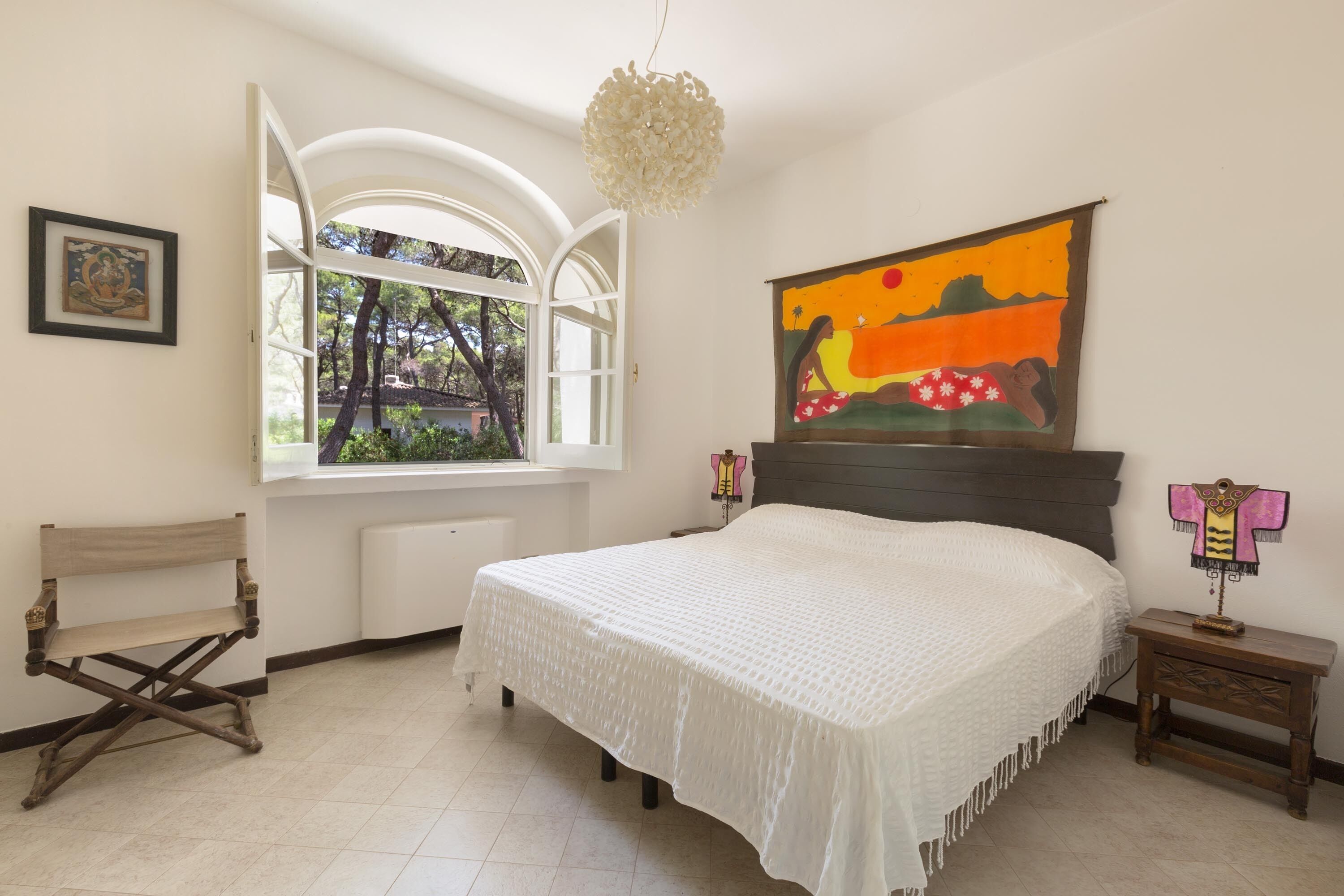 A bedroom with a bed, a window, a bench, and a painting on the wall.