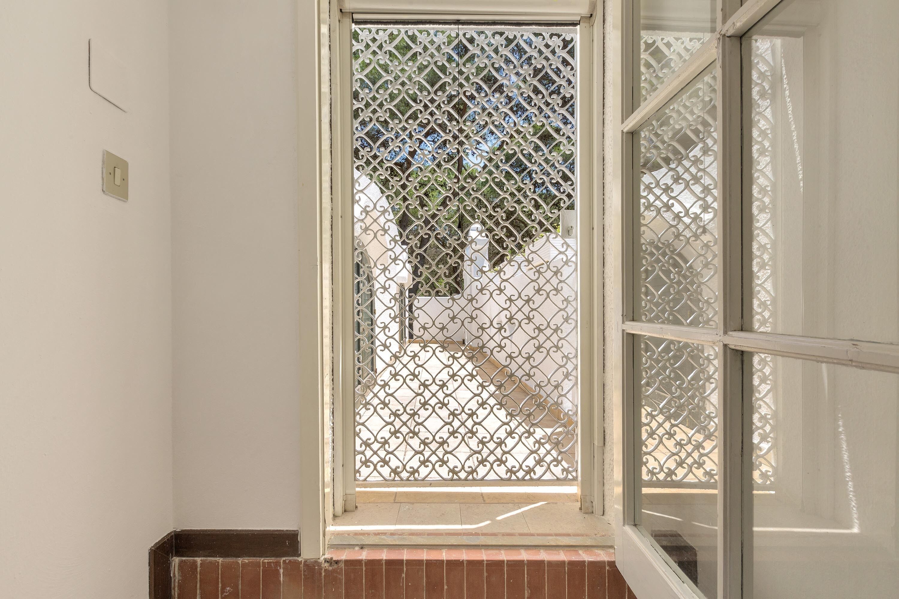 Habitación con ventana que tiene una celosía metálica decorativa, un enchufe visible y un zócalo de ladrillo.