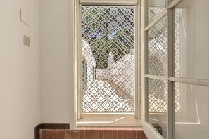 A room with a window featuring a decorative metal screen, a visible electrical outlet, and a brick baseboard. - Villa Denise (Castellaneta)