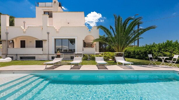 Una casa moderna con piscina, sillas de descanso y un jardín bien cuidado.