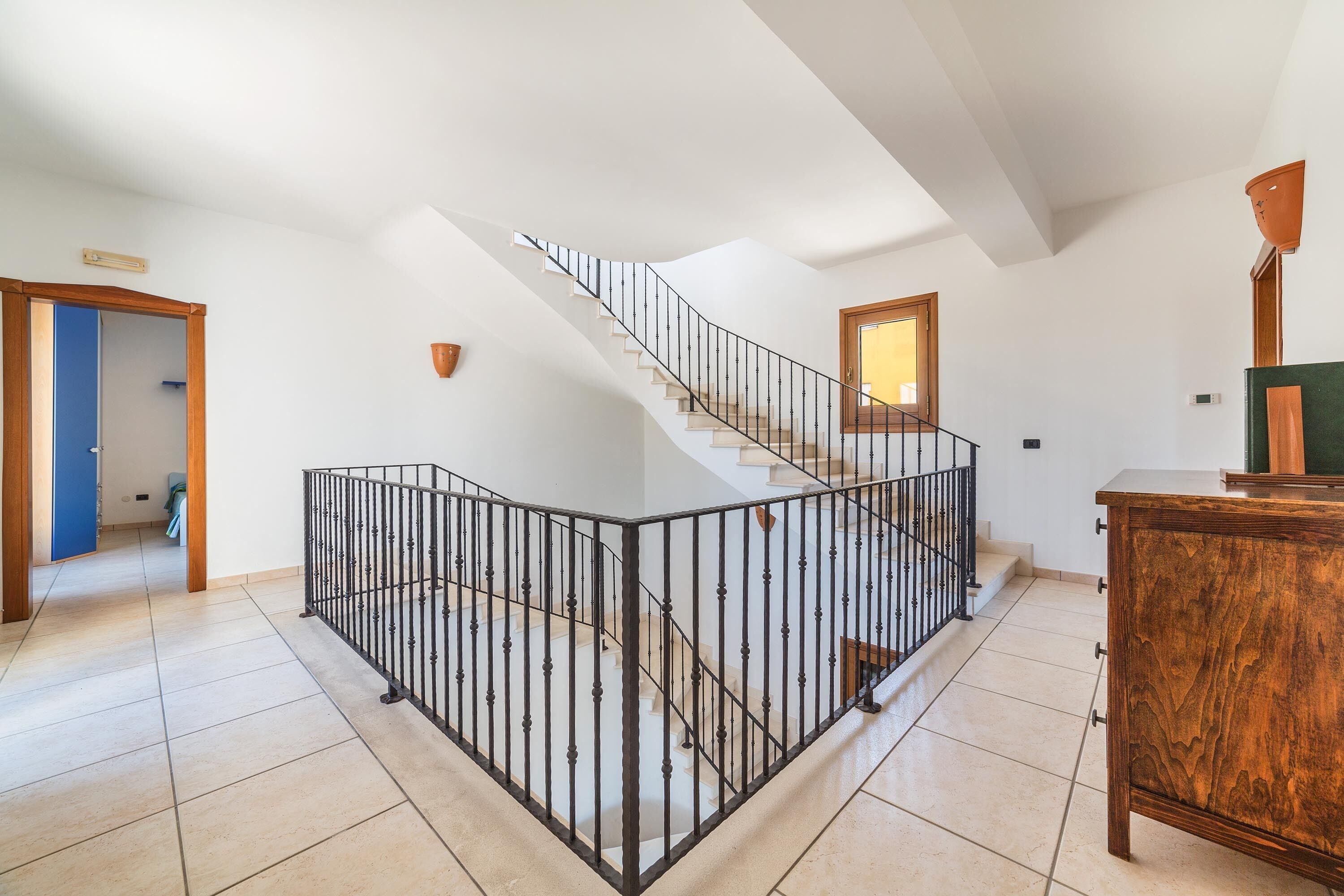 A spacious room with a curved staircase, a wooden cabinet, and a view of the outside.