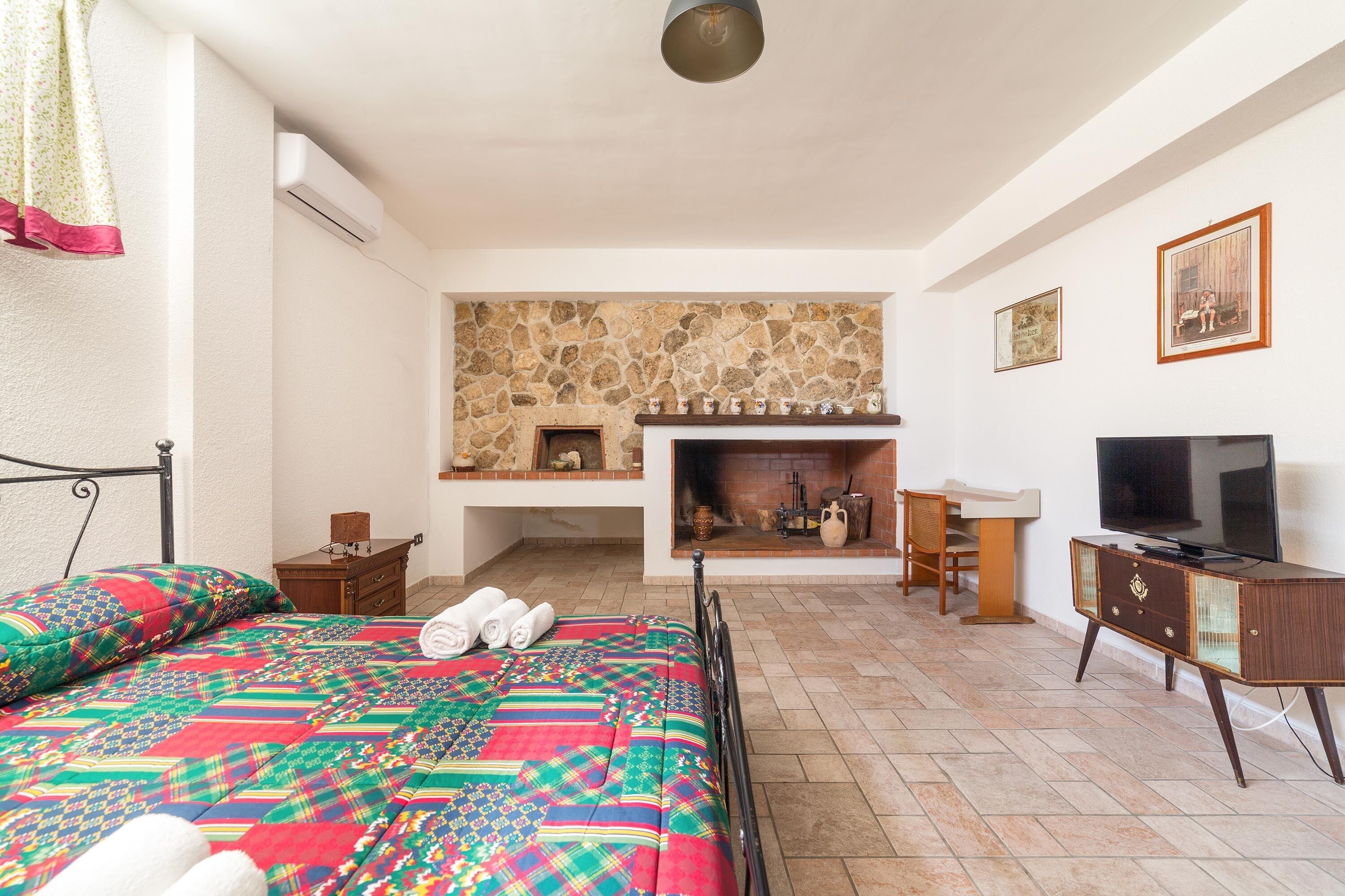 A bedroom with a bed, a television, a fireplace, and a stone wall.
