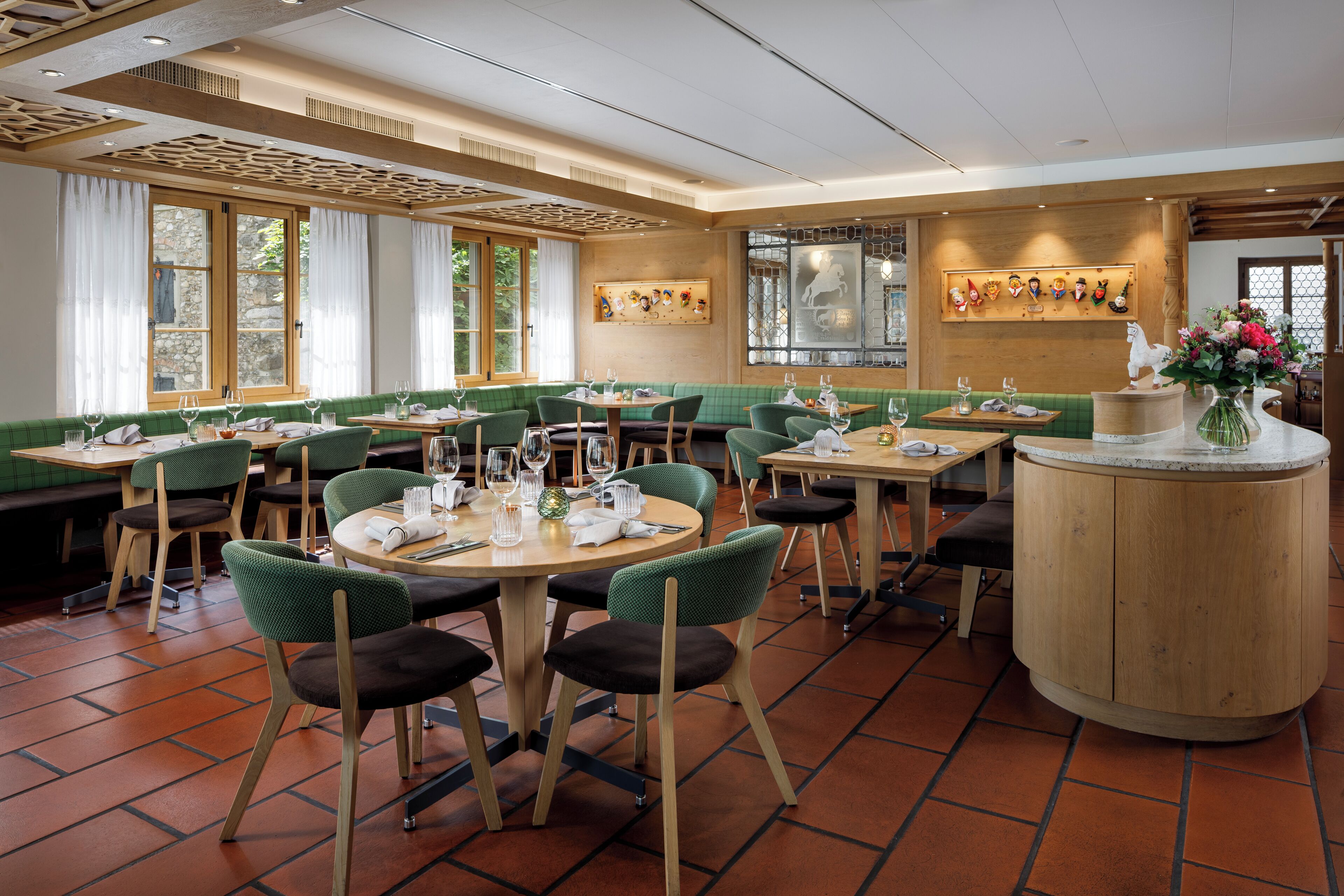 Ein Restaurant mit grünen Sitzbänken, runden Tischen und einer zentralen Holztresen.