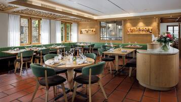 Ein Restaurant mit grünen Sitzbänken, runden Tischen und einer zentralen Holztresen.