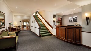 Eine Hottelobby mit einer Treppe, einem Empfangsbereich und einem Essbereich im Hintergrund.