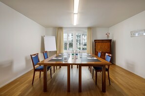 Un salón de conferencias con una mesa de madera, sillas azules, una pizarra y vistas a edificios a través de una puerta de cristal.