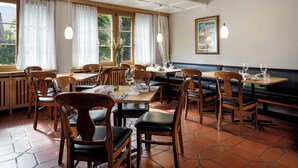 Ein Restaurant mit Holztischen, großen Fenstern und einem Fliesenboden.