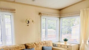 Una habitación acogedora con un sofá color crema, una mesita con cafetera y una ventana con persianas.