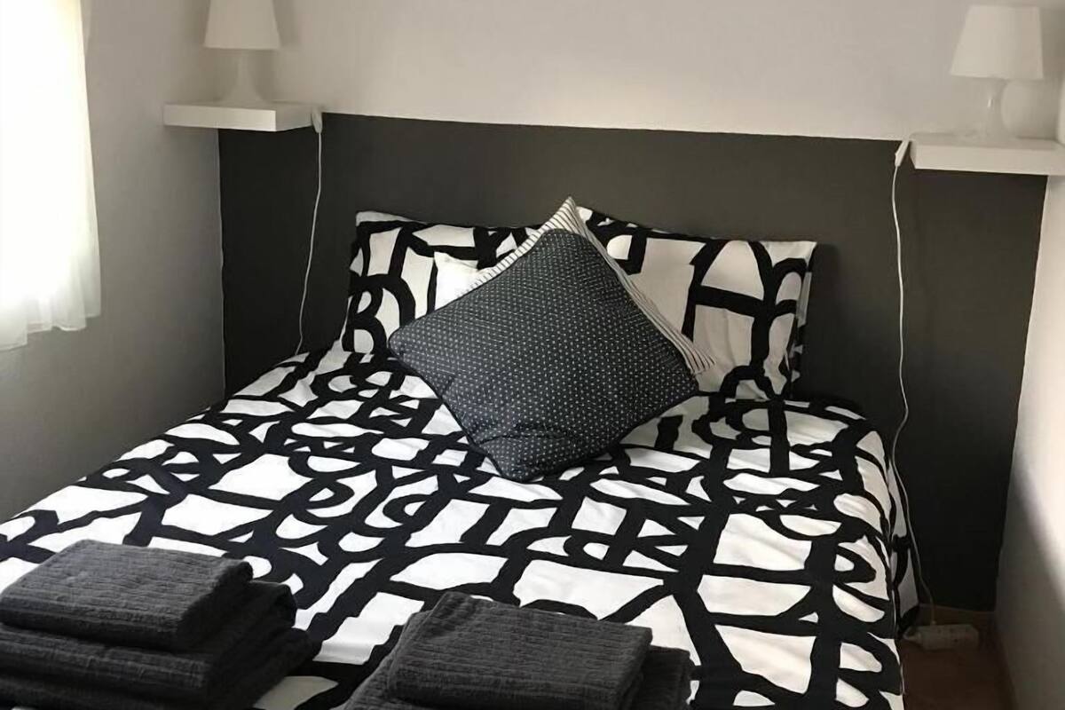 Una cama bien hecha con una colcha de diseño geométrico, dos almohadas y dos mantas dobladas.